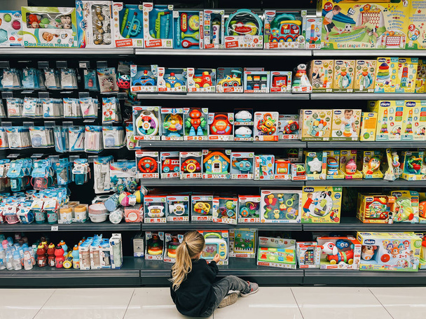Mała dziewczynka wybiera zestaw zabawek siedzących na podłodze w supermarkecie. Wysokiej jakości zdjęcie - Zdjęcie, obraz