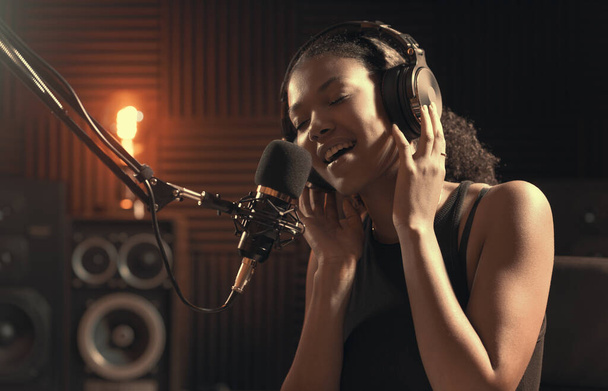 Attractive young woman working in the recording studio, she is singing into a microphone - Valokuva, kuva