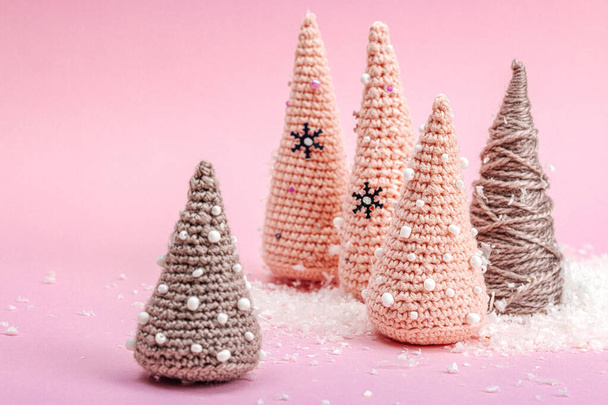 手作りウィンターコンポジション。 かぎ針編みされたクリスマスツリーのセット,ピンクの背景に人工雪. クリエイティブな趣味コンセプト,トップビュー - 写真・画像