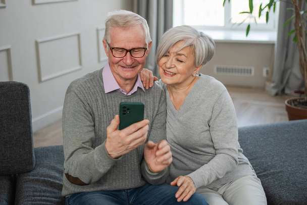 Βίντεο κλήση. Ευτυχισμένο ζευγάρι ηλικιωμένων γυναικών με smartphone που έχουν βιντεοκλήση. Ο ώριμος παππούς της γιαγιάς μιλάει διαδικτυακά. Χρήση σύγχρονης τεχνολογίας παλαιότερης γενιάς. Εικονική συνάντηση σε απευθείας σύνδεση συνομιλία - Φωτογραφία, εικόνα