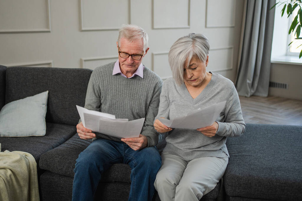 Szomorú, hogy a középkorú idős házaspár papírral ül. Boldogtalan idősebb férfi nő olvasás papír számla kezelése banki pénzügyek kiszámítása adók tervezés hitel adósság nyugdíjkifizetés - Fotó, kép