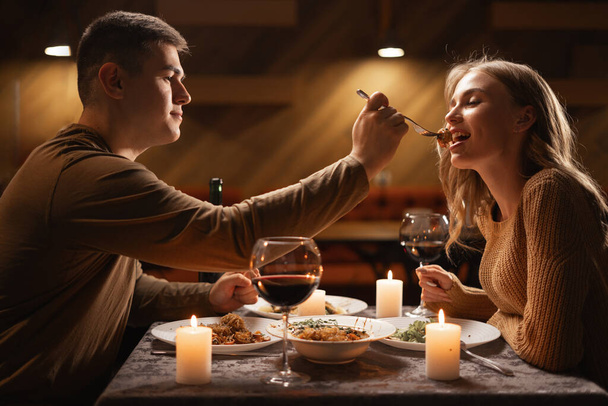 Relation amoureuse. Couple amoureux dîner dans un café. Un homme souriant nourrit sa femme. Célébration de la Saint-Valentin concept - Photo, image