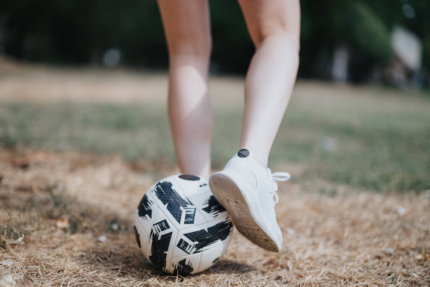Een atletische vrouw traint buiten, toont haar fit lichaam onder het genot van een zonnige dag in het park en indrukwekkende voetbal freestyling vaardigheden en jongleren vaardigheden. - Foto, afbeelding