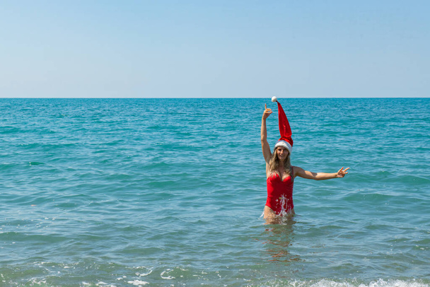 Zabawa nad morzem: dziewczyna w czerwonym stroju kąpielowym i Santa Hat. Wysokiej jakości zdjęcie - Zdjęcie, obraz