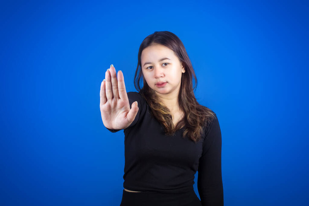 Не надо. Обеспокоенная азиатка показывает знак неприятия, говорит нет, повышает осведомленность, стоя на синем фоне - Фото, изображение