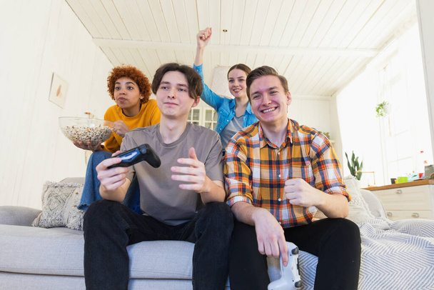 Πάρτι. Χαρούμενη ομάδα φίλων που παίζουν βιντεοπαιχνίδια στο σπίτι. Ευτυχισμένοι διαφορετικοί φίλοι που διασκεδάζουν μαζί σε εσωτερικούς χώρους. Ψυχαγωγία της φιλίας. Νέοι καλύτεροι φίλοι απολαμβάνουν το Σαββατοκύριακο - Φωτογραφία, εικόνα