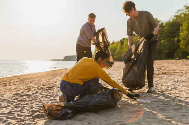Aardedag. Vrijwilligers activisten verzamelen vuilnis schoonmaken van strand kustzone. Vrouwen en mannen doen plastic afval in vuilniszakken aan de kust van de oceaan. Milieubehoud kustreiniging - Foto, afbeelding