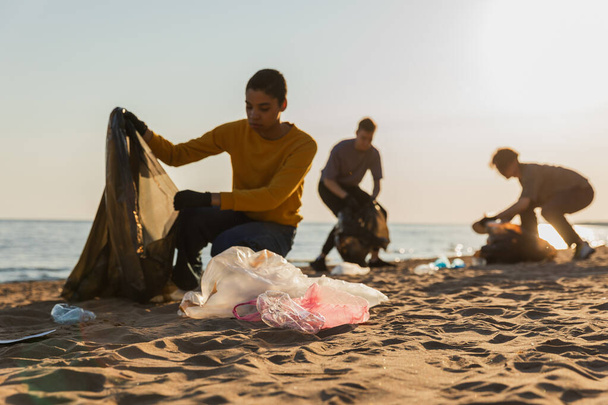Dia da Terra. Ativistas voluntários recolhem limpeza de lixo da zona costeira da praia. Mulher homem com lixo no saco do lixo na costa do oceano. Conservação ambiental limpeza da zona costeira. Imagem turva - Foto, Imagem