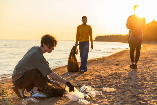 Dia da Terra. A equipe de ativistas voluntários coleta a limpeza do lixo da zona costeira da praia. Mulher homem coloca lixo plástico no saco de lixo na costa do oceano. Conservação do ambiente limpeza da zona costeira - Foto, Imagem