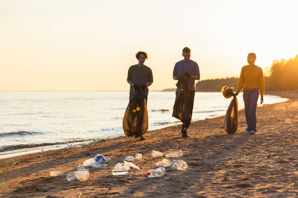 Aardedag. Vrijwilligers activisten team verzamelt vuilnis reinigen van strand kustzone. Vrouwen met vuilnis in vuilniszak aan de kust. Milieubehoud kustreiniging - Foto, afbeelding