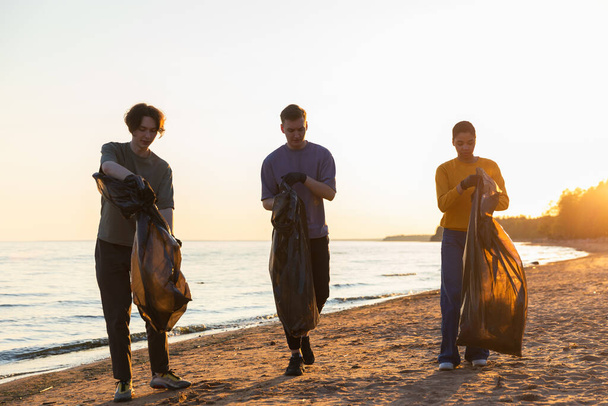 Den Země. Dobrovolnický tým aktivistů sbírá odpadky z pobřežní zóny na pláži. Ženy s odpadky v pytli na pobřeží oceánu. Ochrana životního prostředí čištění pobřežních zón - Fotografie, Obrázek