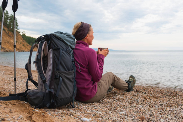 ハイキング観光アドベンチャー。 バックパッカーの女性は,美しい景色を見ながらハイキングした後に休んでいます. 湖の近くに座っているバックパックを持つハイカーガールの女性観光客. ハイカー女性はハイキング観光アクティブ休暇を楽しむ - 写真・画像