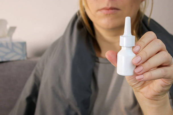 Primer plano de la mujer que sostiene un aerosol blanco de la nariz de la botella, fondo borroso con espacio de copia - Foto, imagen