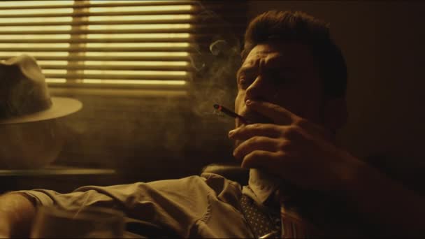 Close-up sepia beelden van gefrustreerde bebaarde blanke man die diep in gedachten zit en 's avonds sigaretten rookt en drank drinkt in zijn appartement. - Video