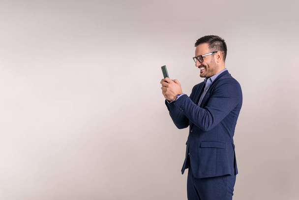 Lachende jonge zakenman doet social media marketing via mobiele telefoon tegen een witte achtergrond - Foto, afbeelding
