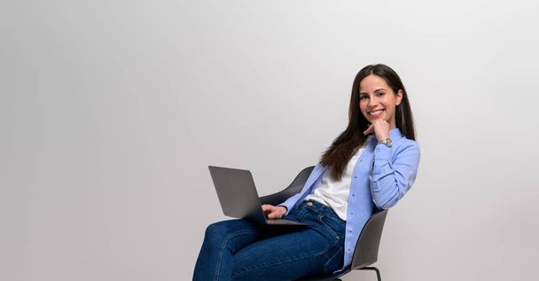 Портрет впевненої усміхненої жінки-професіонала з ноутбуком, що сидить на стільці на білому тлі - Фото, зображення