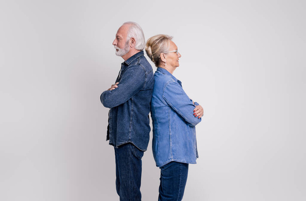 Boční pohled na starší pár se zkříženýma rukama stojící zády k sobě a ignorující na bílém pozadí - Fotografie, Obrázek