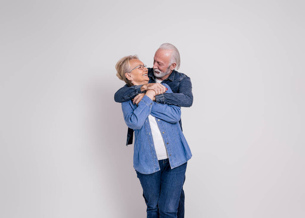 Romantische Senior Ehemann umarmt und sieht lächelnde Frau von hinten vor weißem Hintergrund - Foto, Bild