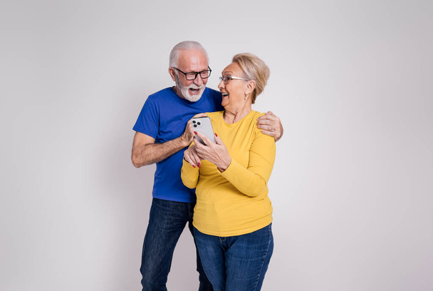 Feliz pareja de ancianos gritando y mirándose el uno al otro después de leer buenas noticias sobre fondo blanco - Foto, imagen