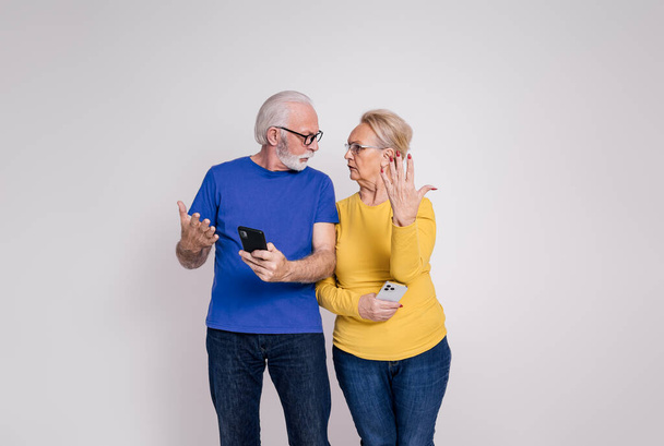 Απογοητευμένο ζευγάρι τελειόφοιτων με έξυπνα τηλέφωνα να ερωτοτροπεί και να τσακώνεται μεταξύ τους σε λευκό φόντο - Φωτογραφία, εικόνα