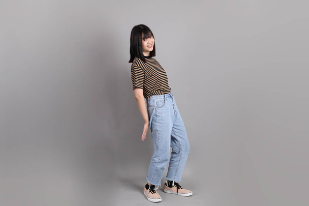 Plná délka mladé dospělé asijské ženy stojící na šedém pozadí. - Fotografie, Obrázek