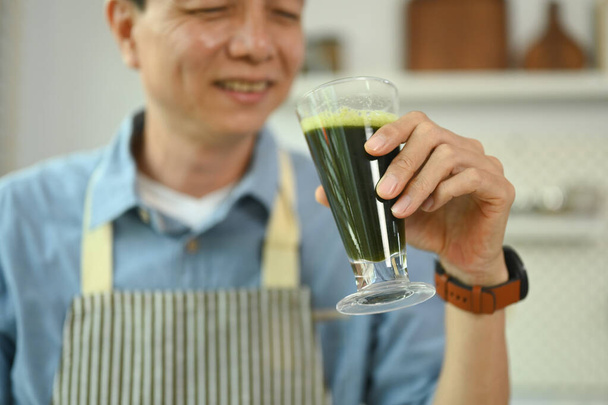 Feliz hombre de mediana edad bebiendo un batido verde saludable en la mañana en casa - Foto, imagen
