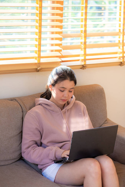 Business asian casual woman typing on laptop sitting on sofa in cozy home office information technology - Фото, зображення