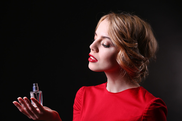 Beautiful young woman with perfume bottle on black background - Photo, image
