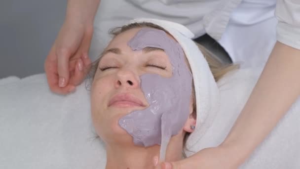  Un cosmetólogo aplica una máscara a la cara de un paciente en una clínica de cosmetología, limpieza facial profesional, pelado de la piel, concepto de cosmetología. - Metraje, vídeo
