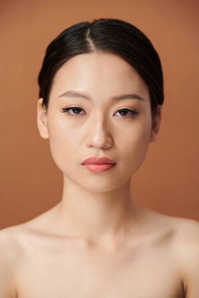 Serious young Asian woman with eye liner and lip tint looking at camera - 写真・画像