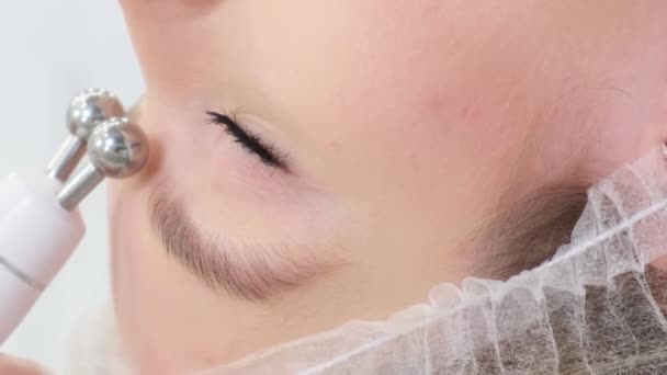 Een close-up van een schoonheidsspecialiste die een stimulerende gezichtstherapie uitvoert genaamd gezichtsmicrostroom. Cosmetische verzorging van een vrouwelijk gezicht. Verticale video. - Video
