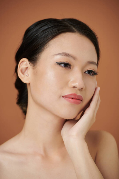 Портрет задумчивой азиатской девушки и прикосновение к ее мягкой коже - Фото, изображение