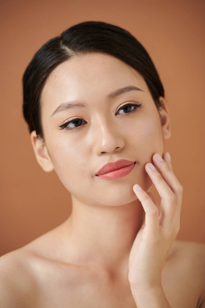 Studio portrait of pensive young woman touching her soft tender skin after spa procedure - Photo, Image