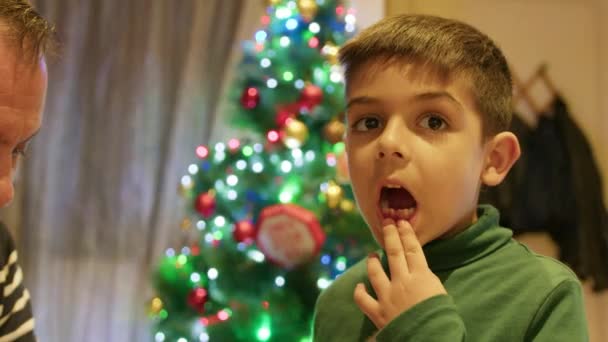 Un ragazzo carino che ha appena estratto il dente lattiginoso mostrando lo spazio davanti all'albero di Natale. Filmati 4k di alta qualità - Filmati, video