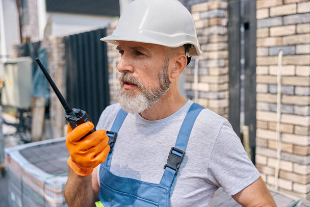 Portrait of serious builder in hard hat talking over two-way radio outdoors - Foto, imagen