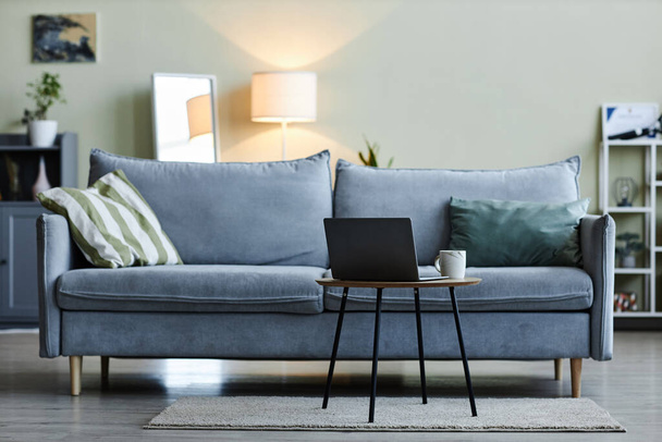 Hintergrundbild der gemütlichen blaugrauen Couch im minimalen Wohnzimmer mit Laptop auf Couchtisch, Kopierraum - Foto, Bild