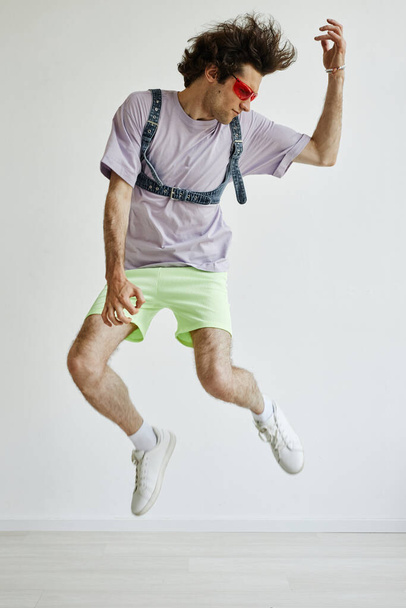 Függőleges akció lövés a fiatal férfi ugrás a levegőben visel színes ruhát - Fotó, kép
