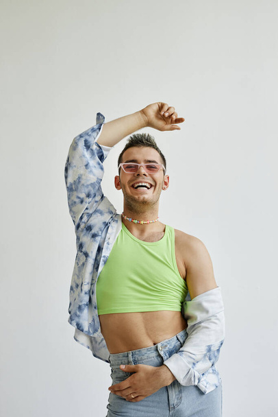 Vertikales Porträt eines jungen schwulen Mannes, der vor weißem Hintergrund tanzt und glücklich lächelt - Foto, Bild
