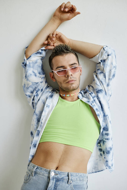 Retrato vertical del hombre gay confiado posando sensualmente apoyado contra la pared blanca - Foto, Imagen