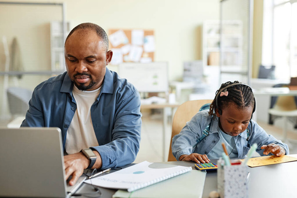 Visão frontal retrato de pai solteiro preto trabalhando em casa com a criança brincando com calculadora ao lado dele - Foto, Imagem