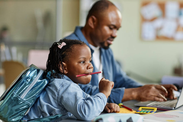 Вид сбоку портрет милой черной девушки, играющей с карандашами, в то время как отец работает в фоновом режиме - Фото, изображение