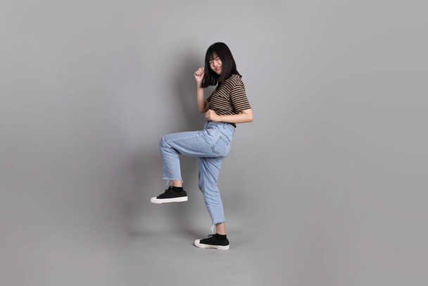 La longitud completa de la joven mujer asiática adulta de pie sobre el fondo gris. - Foto, Imagen