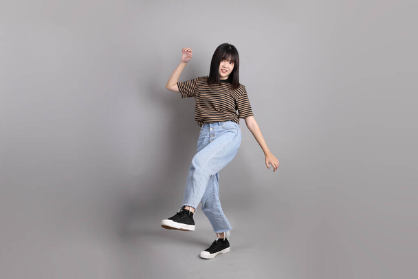 The full length of young adult Asian woman standing on the grey background. - Photo, Image