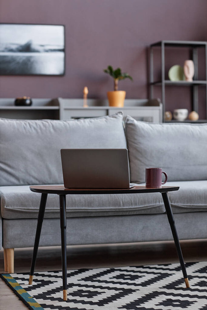 Vertikales Hintergrundbild von offenem Laptop durch bequeme Couch im eleganten Wohnbereich mit lila Wand - Foto, Bild