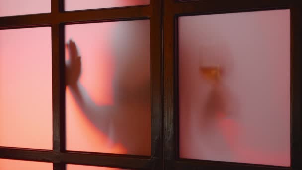 Rätselhaftes Bild eines unerkannten Nacktmodells mit einem Glas Wein hinter mattem Glas bei Sonnenuntergang. Verführerisches Mädchen, junge, flexible Frau mit perfektem Körper, beweglicher Silhouette. Langsames und qualitativ hochwertiges 4k-Filmmaterial - Filmmaterial, Video