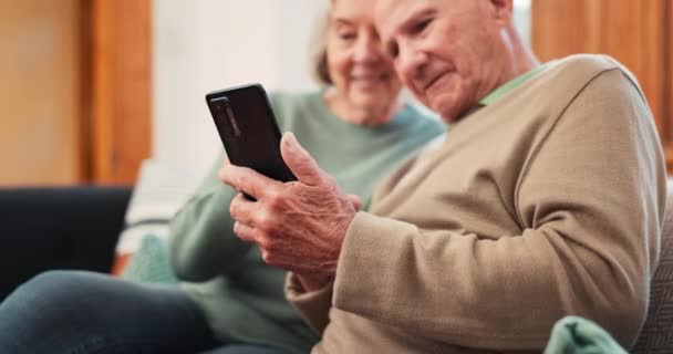 Ηλικιωμένο ζευγάρι, χαλαρώστε και διαβάστε στον καναπέ με τηλέφωνο, εφαρμογή ή streaming βίντεο στα μέσα κοινωνικής δικτύωσης με το διαδίκτυο. Κύλιση, κινητό τηλέφωνο ή άτομα σε συνταξιοδότηση με online ειδήσεις, ιστοσελίδα ή θέση στο σαλόνι. - Πλάνα, βίντεο