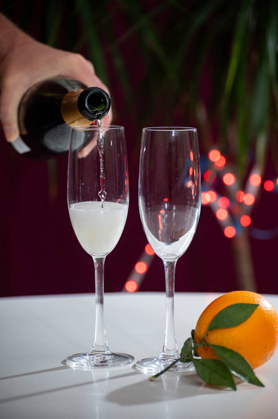 Nalanie brutalnego szampana, wina cava lub prosecco w kieliszkach z lampkami girlandowymi na ciemnym tle, na przyjęciu noworocznym lub urodzinowym - Zdjęcie, obraz