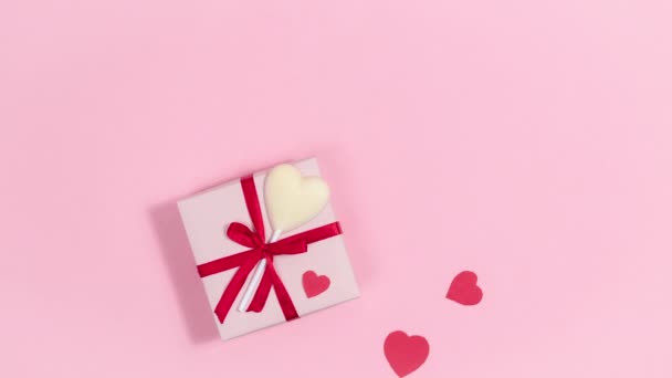 4k Κοντά σε ροζ κουτί δώρου με κόκκινη κορδέλα και λευκή σοκολάτα καραμέλα καρδιά, καρδιές πετούν από, σύμβολα της αγάπης. Ευχετήρια κάρτα για την ημέρα του Αγίου Βαλεντίνου. Ροζ φόντο. Αντιγραφή χώρου. Επίπεδη. Σταμάτημα κίνησης - Πλάνα, βίντεο