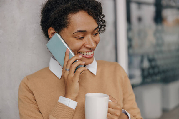 Χαμογελώντας γυναίκα ελεύθερος επαγγελματίας μιλάει τηλέφωνο με τον πελάτη, ενώ στέκεται σε συνεργασία φόντο - Φωτογραφία, εικόνα