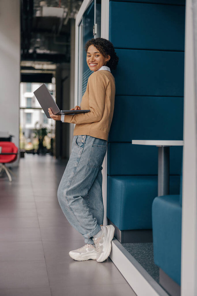 Pretty kobieta freelancer pracuje na laptopie, stojąc na nowoczesnym tle współpracowników - Zdjęcie, obraz